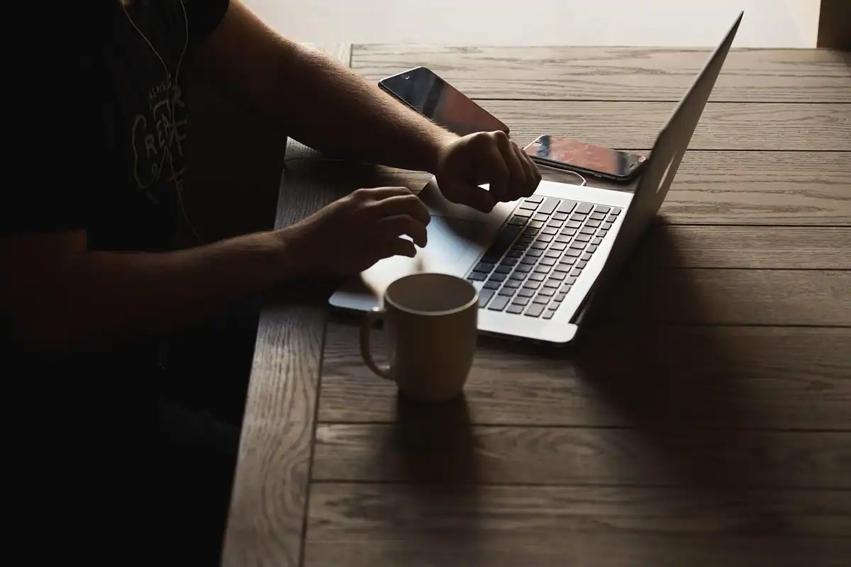 Persoană care tastează pe un laptop, lângă o cană pe masă