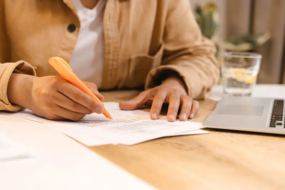 Persoană subliniază cu un marker portocaliu un text printat, la birou