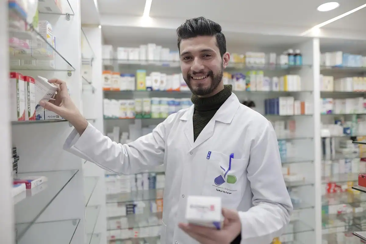 Farmacist zâmbitor ține o cutie de medicament lângă rafturile farmaciei