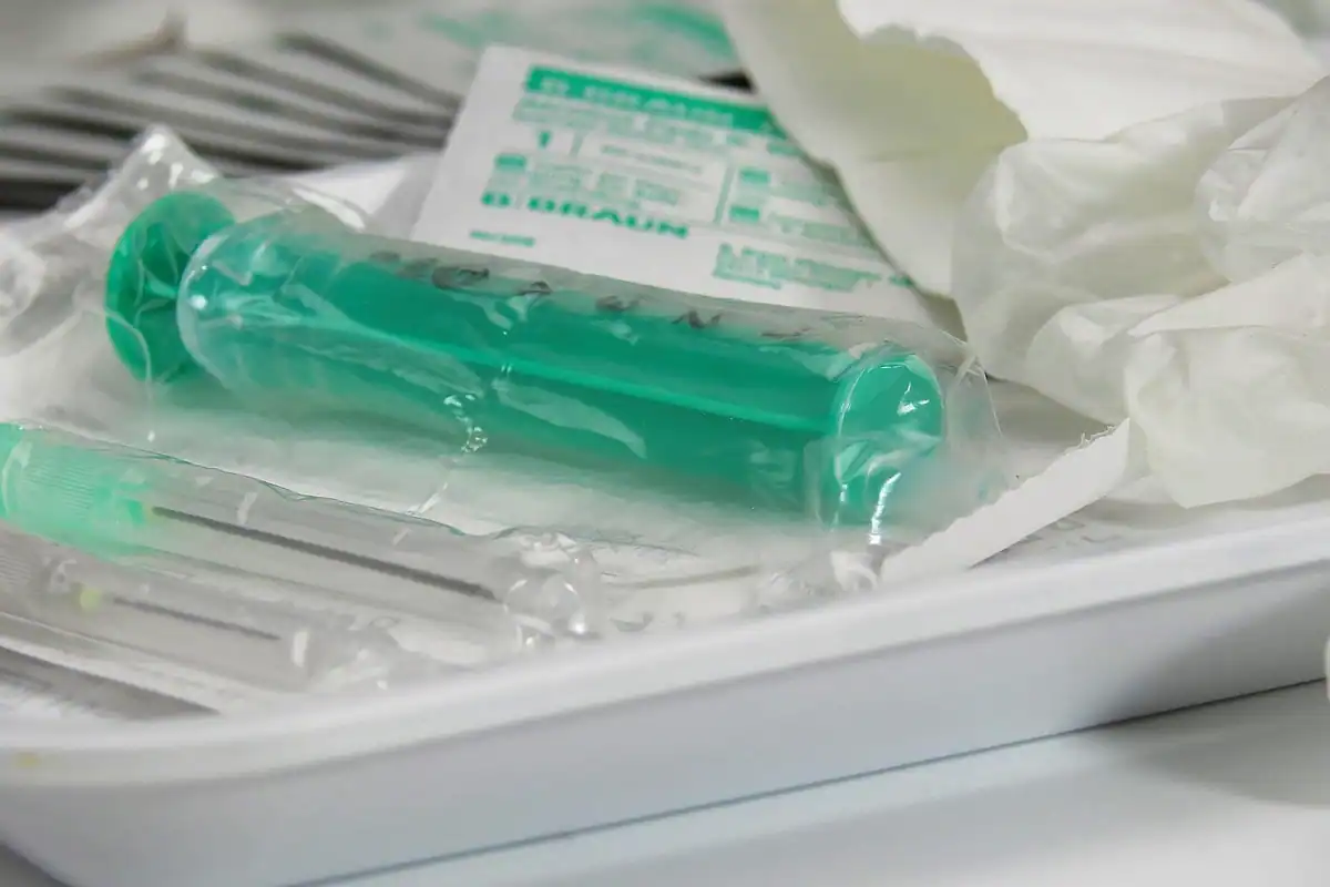 Seringi și ace sterile în ambalaje, așezate pe o tavă medicală