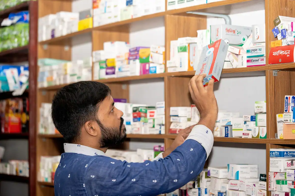 Farmacist verifică o cutie de medicament în fața unui raft plin