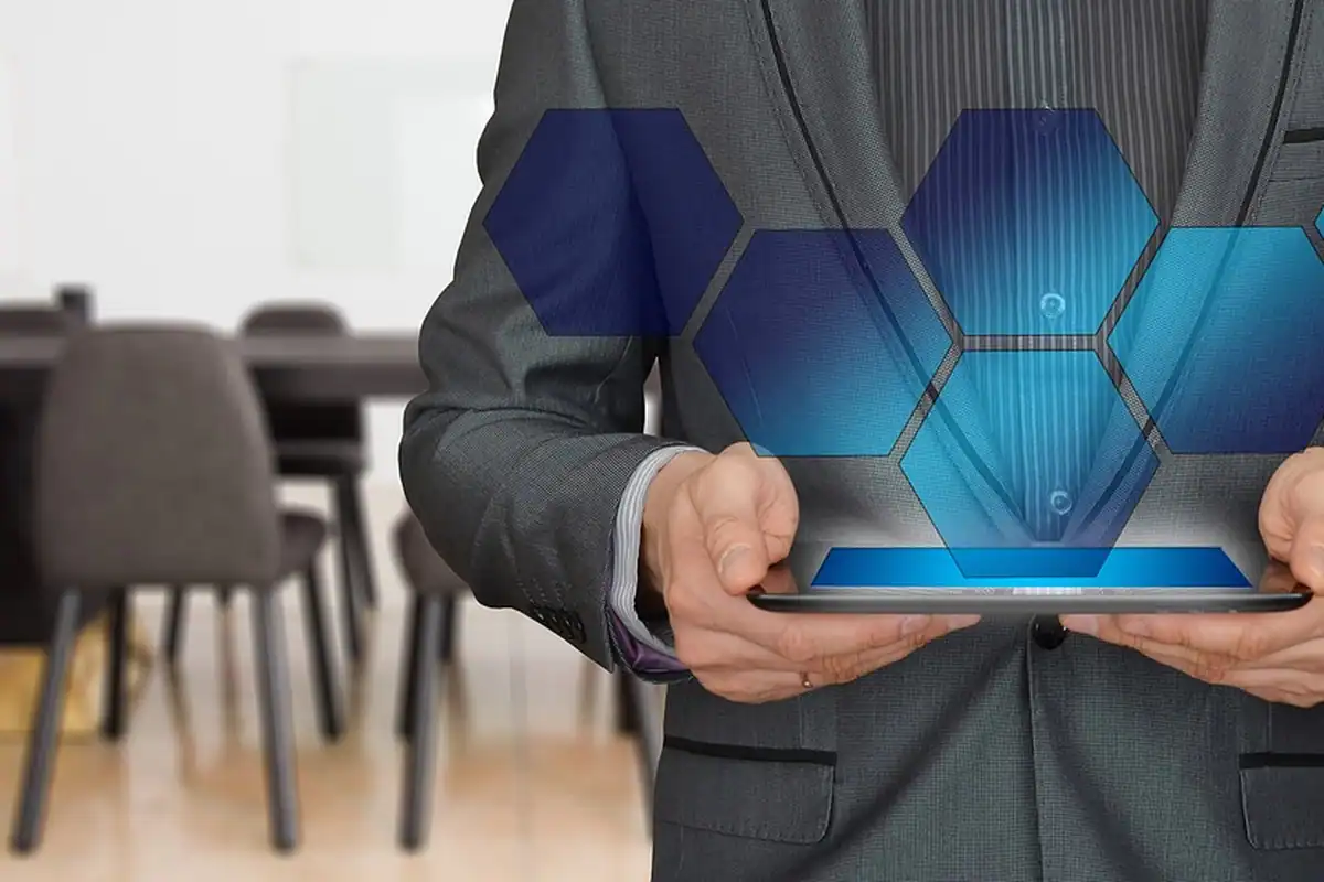 Bărbat în sacou ține o tabletă pe care plutesc hexagoane luminoase