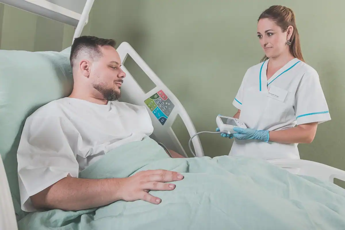 Pacient în pat de spital, lângă o asistentă care îi notează datele