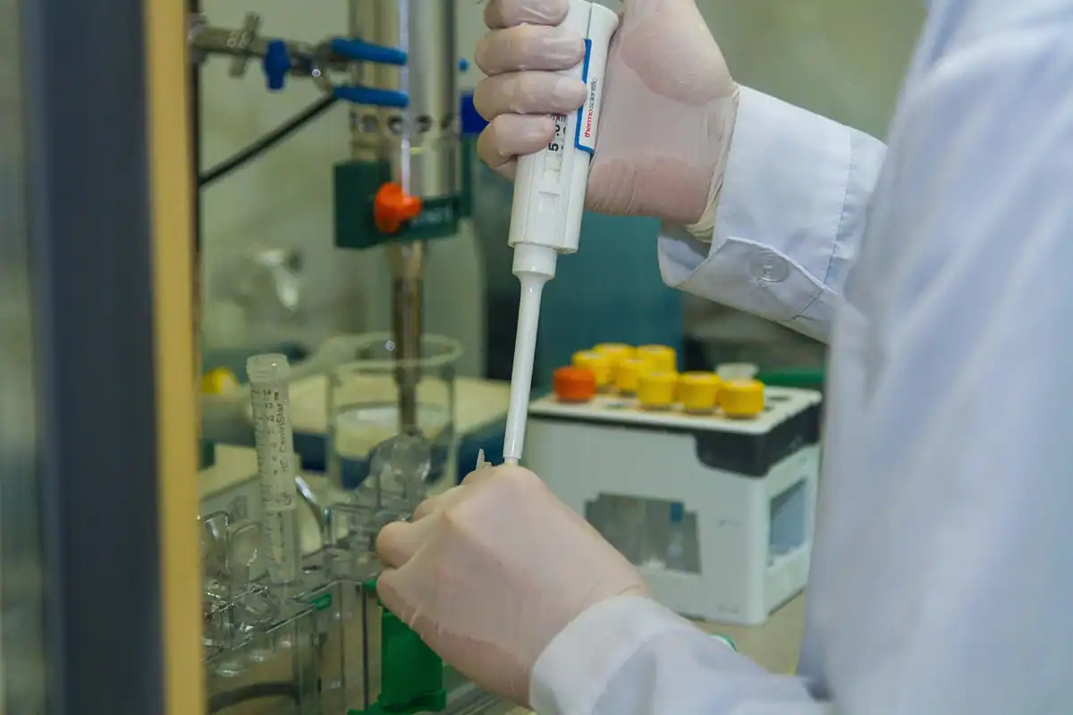 Mână cu mănușă pipetează o probă într-un montaj de laborator