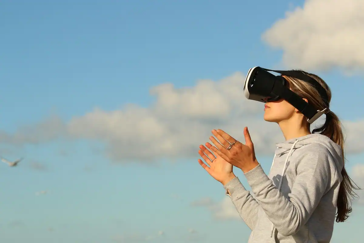 Femeie cu ochelari de realitate virtuală, cu brațele deschise sub cer