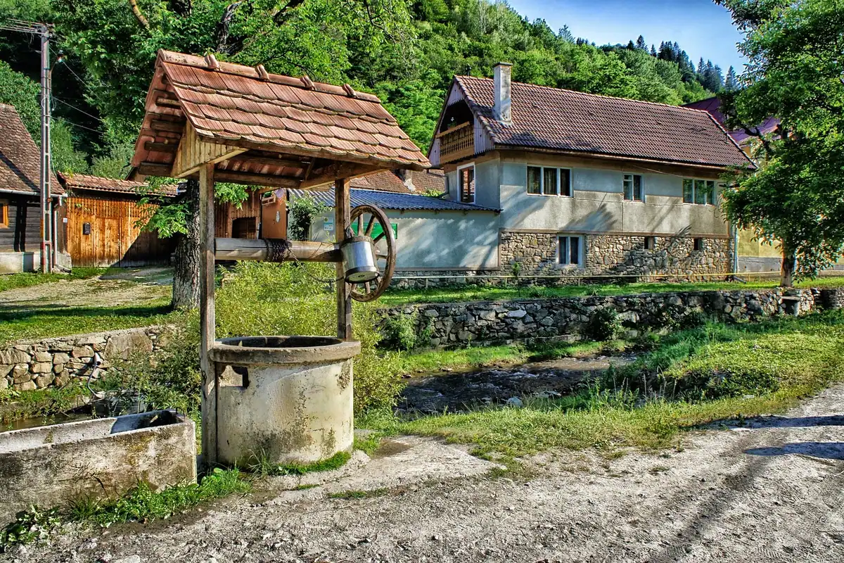 Fântână cu acoperiș și case de lemn într-un sat de la țară